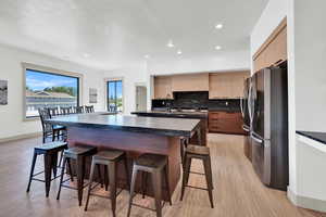 Kitchen featuring light wood-type flooring, decorative backsplash, a kitchen breakfast bar, stainless steel refrigerator, and a center island with sink