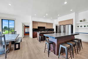 Kitchen with stainless steel refrigerator, tasteful backsplash, light hardwood / wood-style floors, a kitchen island with sink, and a breakfast bar