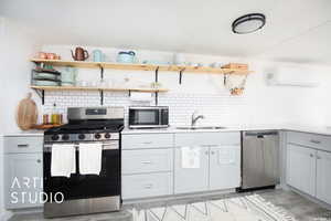 Kitchen with appliances with stainless steel finishes, sink, backsplash, light hardwood / wood-style floors, and a wall mounted AC