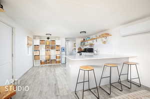 Kitchen with an AC wall unit, kitchen peninsula, backsplash, a kitchen bar, and light hardwood / wood-style floors