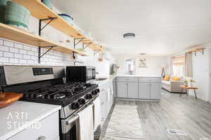 Kitchen featuring kitchen peninsula, backsplash, appliances with stainless steel finishes, gray cabinetry, and light hardwood / wood-style floors