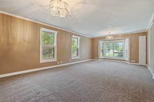 Empty room featuring a notable chandelier, a textured ceiling, carpet, and crown molding