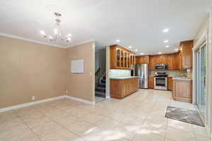 Kitchen with appliances with stainless steel finishes, sink, pendant lighting, ornamental molding, and a chandelier