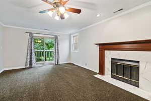 Unfurnished living room with ornamental molding, a high end fireplace, dark colored carpet, and ceiling fan