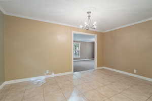 Empty room featuring ornamental molding, a notable chandelier, a textured ceiling, and light tile patterned floors