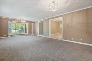 Carpeted empty room with a notable chandelier, ornamental molding, and a textured ceiling