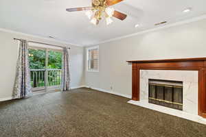 Unfurnished living room featuring crown molding, a high end fireplace, dark carpet, and ceiling fan