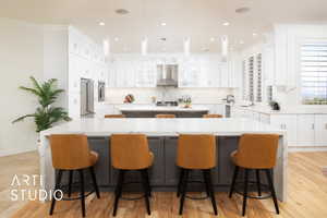 Kitchen featuring two large islands with marble waterfall countertops, chimney range hood, light hardwood / wood-style flooring, pendant lighting, and sink