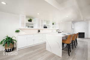 Bar area featuring a premium fireplace, light hardwood / wood-style flooring, white illuminated cabinetry, and island