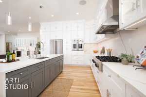 Kitchen featuring wall chimney range hood, hanging light fixtures, white cabinetry, light hardwood / wood-style floors, and stainless steel appliances