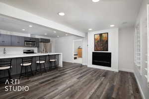 Kitchen featuring sink, stainless steel appliances, gray cabinets, dark wood-type flooring, kitchen island and gas fireplace.