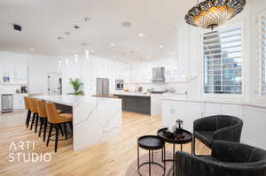 Kitchen with appliances with stainless steel finishes, a kitchen breakfast bar, a large island, white cabinetry, and wall chimney exhaust hood