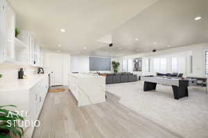 Sports bar with light stone countertops, backsplash, waterfall island, white cabinets, and light hardwood / wood-style flooring