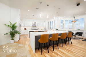 Kitchen with a spacious island, wall chimney exhaust hood, pendant lighting, and white cabinets