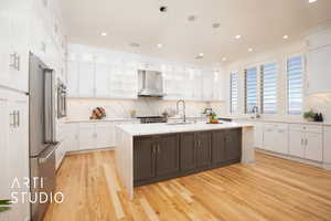 Kitchen featuring appliances with stainless steel finishes, sink, wall chimney exhaust hood, white cabinets, and a kitchen island with sink