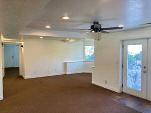 Interior space featuring ceiling fan, a textured ceiling, a wealth of natural light, and dark carpet