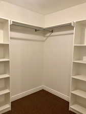 Walk in closet featuring dark carpet his and hers