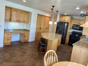 Kitchen with light stone countertops, black appliances, decorative light fixtures, and a kitchen island. HickoryCabinets