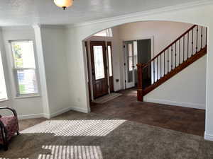 Foyer entrance with a textured ceiling, ornamental molding, and dark colored carpet