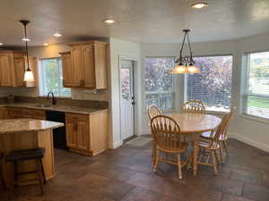 Kitchen featuring black dishwasher, a textured ceiling, light stone countertops, sink, and decorative light fixtures.  Hickory Cabinets