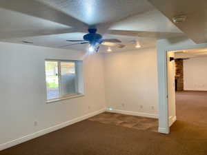 Carpeted empty room featuring a stone fireplace, a textured ceiling, and ceiling fan