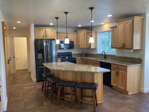 Kitchen with sink, black appliances, a center island, decorative light fixtures, and light stone counters. Hickory Cabinets