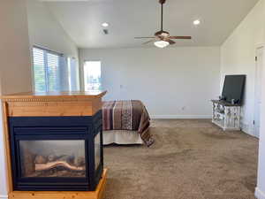 Bedroom featuring ceiling fan, carpet flooring, and vaulted ceiling. Three way fireplace