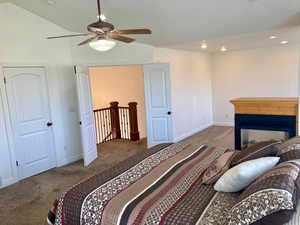 Carpeted bedroom featuring a multi sided fireplace, vaulted ceiling, and ceiling fan