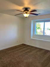 Carpeted empty room featuring a textured ceiling and ceiling fan. Window sea twith storage