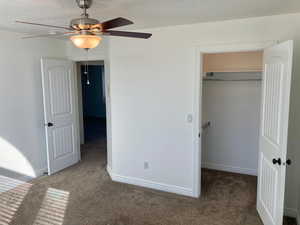 Unfurnished bedroom with dark colored carpet, a closet, a textured ceiling, and ceiling fan. Walk in closet