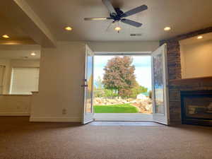 Unfurnished living room with a textured ceiling, a stone fireplace, carpet floors, and ceiling fan