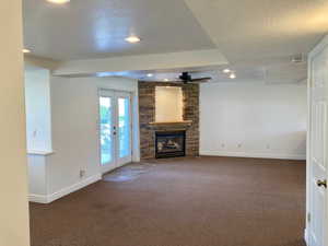 Unfurnished living room featuring dark carpet, french doors, and a stone fireplace