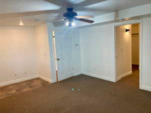 Empty room with ceiling fan, a textured ceiling, and dark carpet