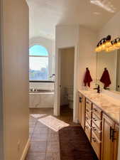 Bathroom featuring lofted ceiling, toilet, vanity, a tub to relax in, and tile patterned flooring