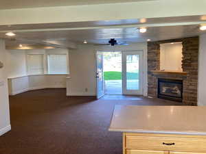 Unfurnished living room featuring a fireplace, a textured ceiling, ceiling fan, beamed ceiling, and dark carpet