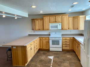 Kitchen featuring a breakfast bar area, kitchen peninsula, light brown Hickory cabinetry, and white appliances included