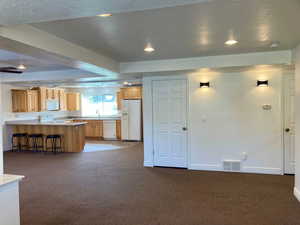 Kitchen with kitchen peninsula, carpet floors, a kitchen bar, and white appliances