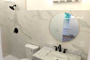 Bathroom featuring toilet, vanity, tile walls, and tiled shower