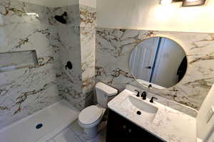 Bathroom with vanity, toilet, tiled shower, and tile walls