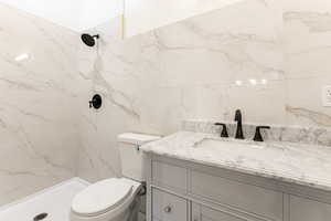 Bathroom featuring tile walls, vanity, a tile shower, and toilet