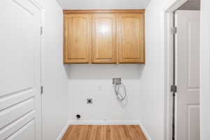 Clothes washing area featuring hookup for a gas dryer, hardwood / wood-style flooring, hookup for a washing machine, hookup for an electric dryer, and cabinets