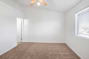 Carpeted spare room featuring ceiling fan and vaulted ceiling