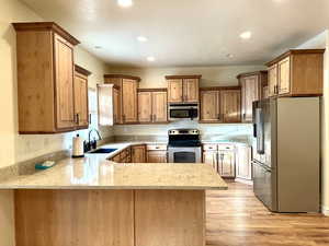 Kitchen with updated cabinets that create an immediate focal point, appliances with stainless steel finishes, light hardwood / wood-style flooring, and handy kitchen peninsula