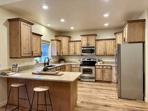 Kitchen featuring kitchen peninsula, a breakfast bar, amazing stainless steel appliances, sink, and light hardwood / wood-style flooring