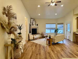 Living room featuring ceiling fan, vaulted ceiling, a tiled fireplace, access to private patio, and light hardwood / wood-style flooring