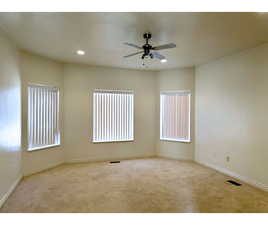 Cozy primary bedroom with light plush carpet, ceiling fan, and windows that stretch across the wall.