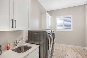 Laundry room featuring cabinets, sink, washing machine and dryer, and light hardwood / wood-style floors