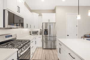 Kitchen featuring white cabinets, decorative light fixtures, stainless steel appliances, and light wood-type flooring