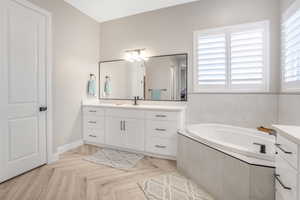 Bathroom featuring vanity, parquet floors, and tiled bath