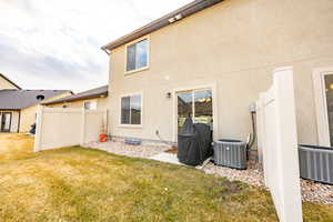 Rear view of property featuring central AC unit, a lawn, fence, and stucco siding